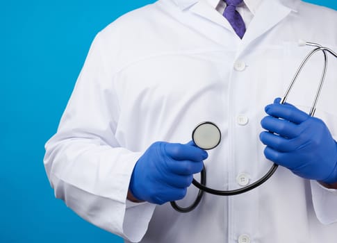 adult male doctor in a white medical coat stands and holds a black stethoscope on a blue background, copy space