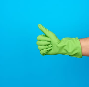 hand in green protective rubber gloves shows gesture like, blue background, positive emotion, consent