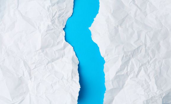 crumpled white sheet of paper torn in two on a blue background. Paper piece torn edge.