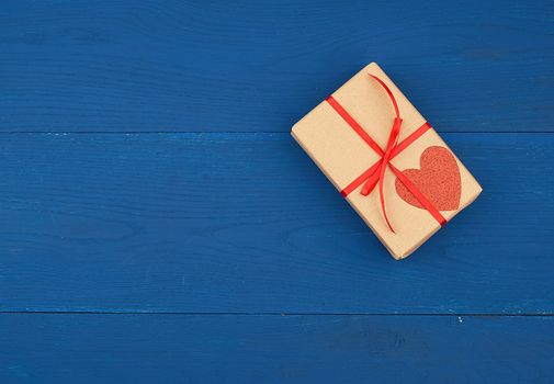 brown box with a gift and a red paper heart tied to a rope, blue wooden background, top view