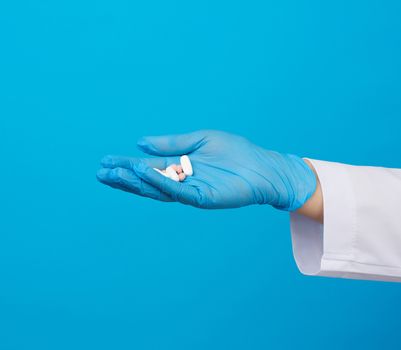 hand with blue sterile gloves holds round pink pills, concept of drug treatment for diseases, blue background