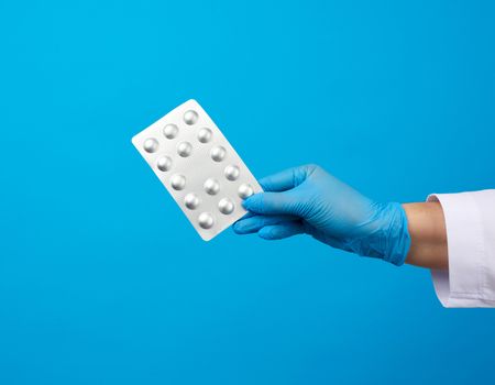 female hand with blue sterile gloves holds a pills in a blister, concept for drug treatment of diseases, blue background