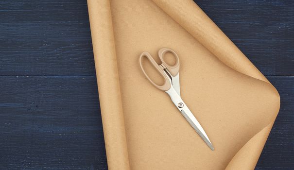 untwisted roll of brown craft paper on a blue wooden background, empty space. Clean sheet, template, angle is twisted