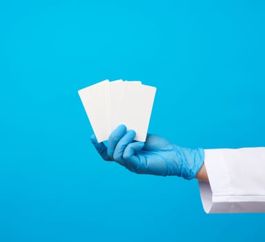 female doctor hand in blue medical latex gloves holds an empty paper business card on a blue background, place for an inscription