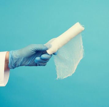 medic woman in white coat holds a twisted textile gauze bandage, blue background, medical item for bandaging human limbs