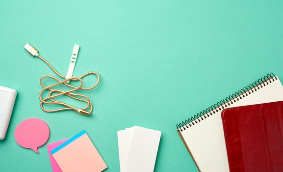 open notebook with blank white sheets, wireless headphones and charger on a green background, top view, copy space