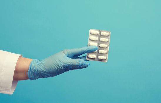 female hand with blue sterile gloves holds a pills in a blister, concept for drug treatment of diseases, blue background