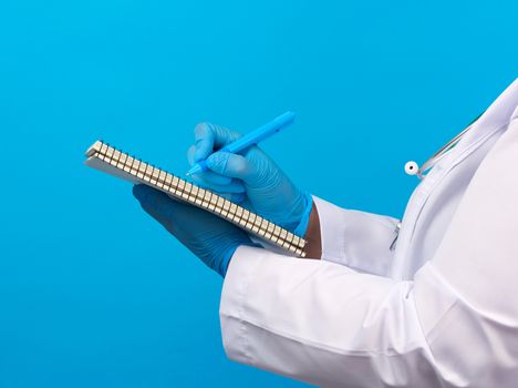 medic woman in white coat, blue latex gloves holding an open notebook with white sheets, blue background, close up