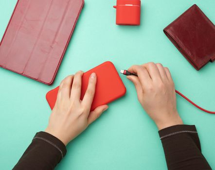 two hands holding a red mobile smartphone and a charging cable on a green background, top view