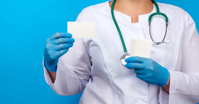 female doctor hand in blue medical latex gloves holds an empty paper business card on a blue background, place for an inscription