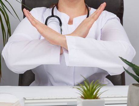 female medic sitting in a brown leather chair in the office and crossed her arms in front of her chest, concept of denial, no