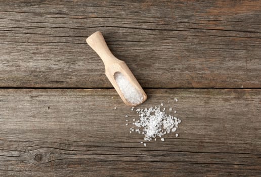 white coarse salt in a wooden spoon, gray table from old boards, top view