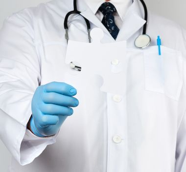 doctor in a white medical coat and blue rubber gloves holds a white paper puzzle, close up