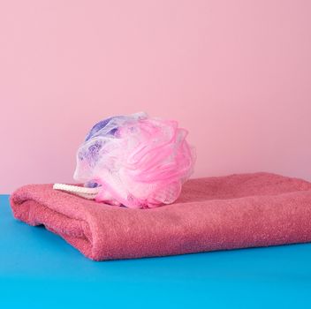stack of pink folded towels and a plastic washcloth on a blue background, bath set