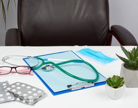 metal stethoscope, paper holder with a blank blue sheet, disposable blue medical mask on a white background, docotor workplace
