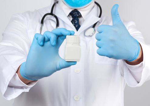 male doctor in a white medical coat and blue latex gloves holds a white plastic jar of pills, close up