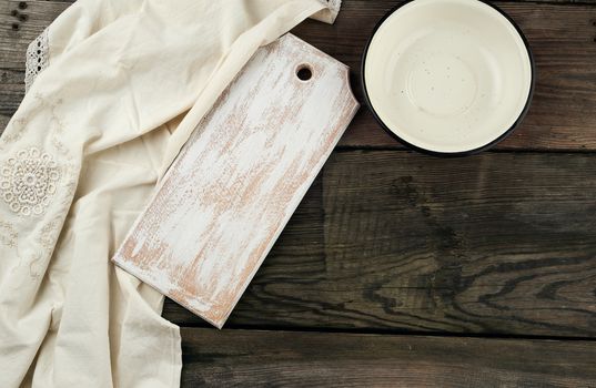 rectangular white cutting kitchen board and empty round plate on a gray wooden background, next to a white textile towel, top view. Copy space