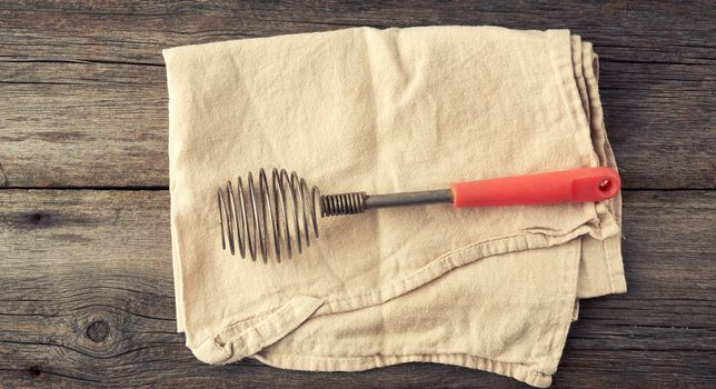 very old kitchen utensil for beating eggs, liquids with a handle on a gray wooden background, top view