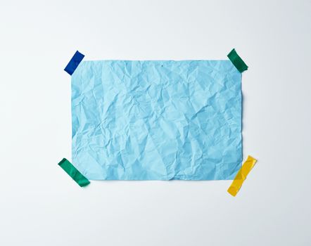 blue crumpled sheet of paper glued with adhesive tape on a white background, place for text