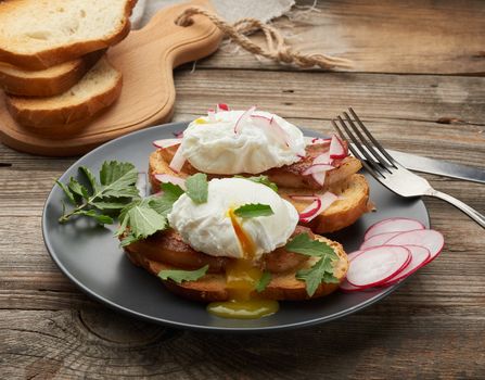 sandwich on toasted white slice of bread with poached eggs, green leaves of arugula and radish, morning breakfast on a gray wooden board, close up