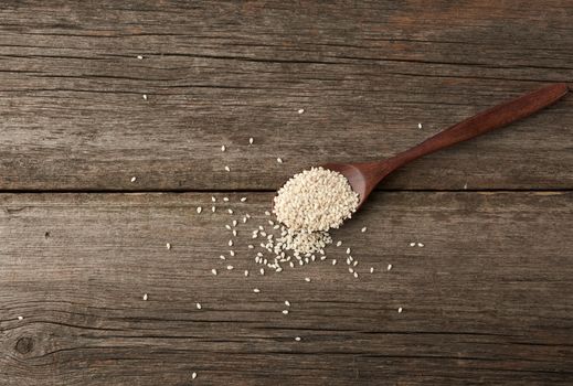dry white sesame seeds in a brown wooden spoon on a gray wooden table from old boards, top view