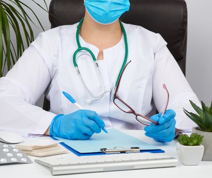 young woman doctor in a white coat, sterile medical gloves writes a prescription on a form, therapist sits on a chair at a white table, workplace