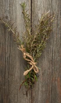 fresh green sprigs of rosemary tied with a brown rope and lie on a gray wooden table from old boards, top view, aromatic spice