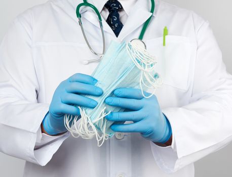 doctor in a white coat, blue latex sterile gloves holds textile medical masks in his hand, protective accessory against viruses and bacteria, close up
