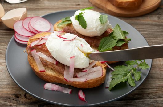 sandwich on toasted white slice of bread with poached eggs, green leaves of arugula and radish, morning breakfast on a gray wooden board, close up