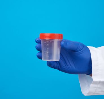 male doctor in a white coat holds a empty plastic container for urine specimen, wearing blue sterile medical gloves