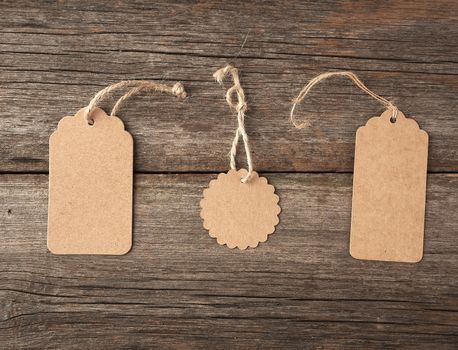 Empty brown paper tag tied with white string. Price, gift, sale tag on the gray wooden background, close up