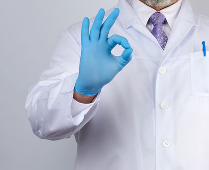 doctor in a white coat with buttons shows a gesture ok with his hands, wearing blue medical gloves, emotion of agreement and approval