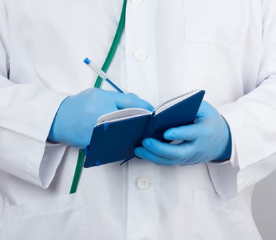 doctor in a white coat and blue gloves holds a blue paper notebook for notes, stethoscope hangs on his neck, white medical backdrop, close up