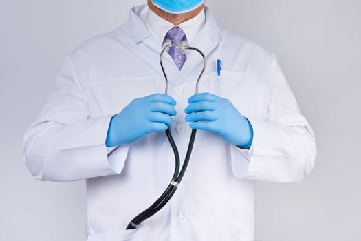 doctor in a white coat and tie holds in his hand a black phonendoscope, wearing blue sterile gloves, white background, medical research