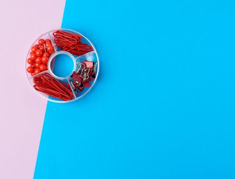 set of stationery, paper clip, clip and buttons in a plastic transparent round box on a colored background, top view