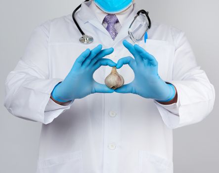 doctor in a white medical coat and blue rubber gloves holds a fresh head of garlic, prevention against viral diseases, traditional medicine