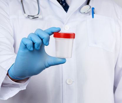 doctor in white uniform and latex gloves is holding an empty plastic container for taking urine samples, close up