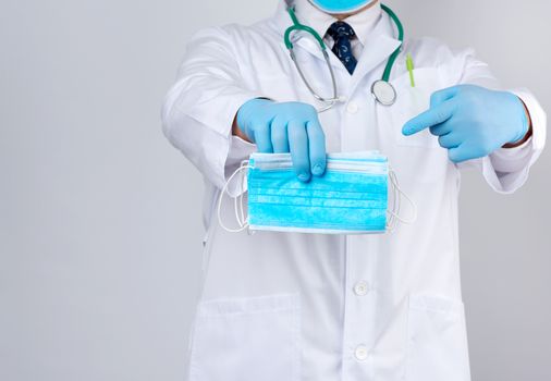 doctor in a white coat, blue latex sterile gloves holds textile medical masks in his hand, protective accessory against viruses and bacteria, copy space