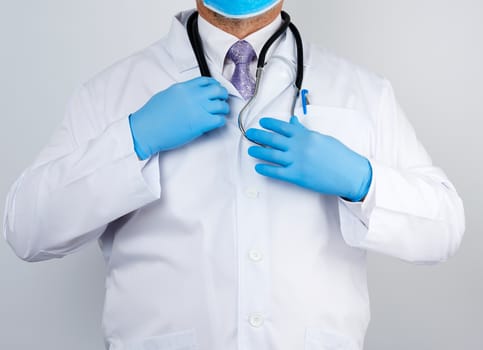 adult male doctor in a white medical coat stands and holds a black stethoscope on a white background, copy space