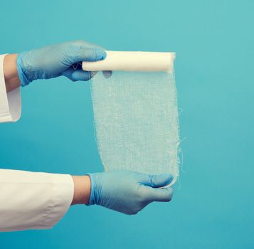 woman in white coat holds a twisted textile gauze bandage, blue background, medical item for bandaging human limbs
