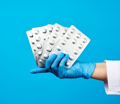 female hand with blue sterile gloves holds a stack pills in a blister, concept for drug treatment of diseases, blue background
