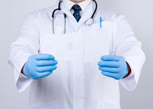 doctor in a white medical coat and blue rubber gloves holds a white paper puzzle, close up