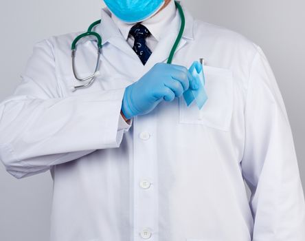 male doctor in a white coat and tie stands and holds a blue silk ribbon in a loop, wearing blue sterile medical gloves, symbol of the fight and treatment of prostate cancer