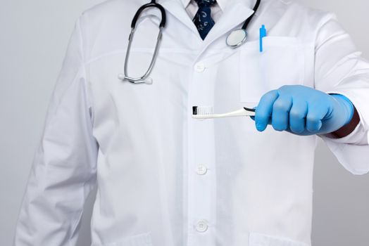 adult doctor therapist is dressed in a white robe uniform and blue sterile gloves is standing and holding a toothbrush, daily brushing concept, white background