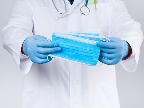 doctor in a white coat, blue latex sterile gloves holds textile medical masks in his hand, protective accessory against viruses and bacteria, close up