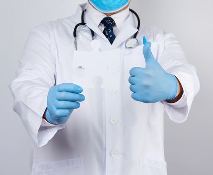 doctor in a white medical coat and blue rubber gloves holds a white paper puzzle, close up