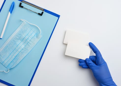 hand in blue medical gloves are holding rectangular white blank business card, top view, white background