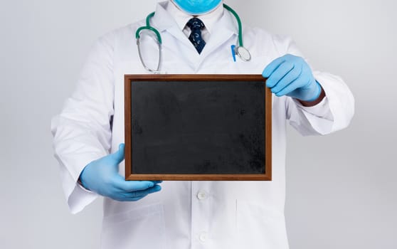 male doctor in a white medical coat and blue latex gloves holds an empty wooden black frame for an inscription, template for a designer