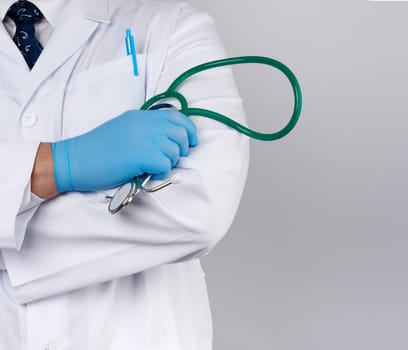 adult male doctor in a white medical coat stands and holds a green stethoscope on a white background, copy space