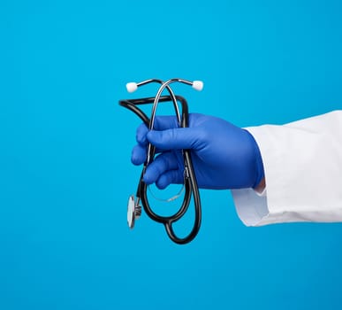 male doctor in a white medical coat holds a black stethoscope on a blue background, copy space
